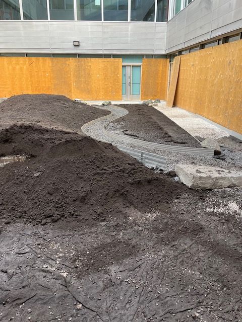 Tas de terre avec un chemin sinueux en construction, près d'un bâtiment au bardage beige et muni d'une porte.