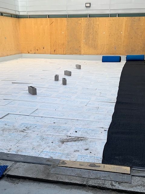 Zone intérieure en travaux. Draps blancs posés, tapis noir, mur en bois, briques, rouleaux bleus.