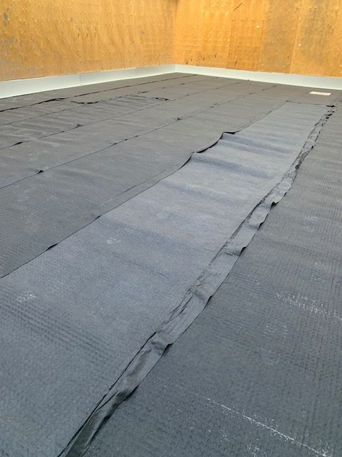 Un tissu noir est étendu sur le sol, recouvrant toute la surface. Un coin de pièce se dessine à l'arrière-plan.