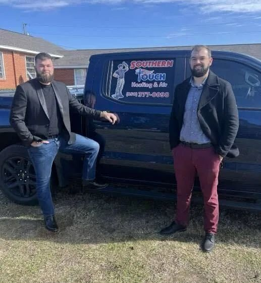 Two men pose by a black truck with company logo for 