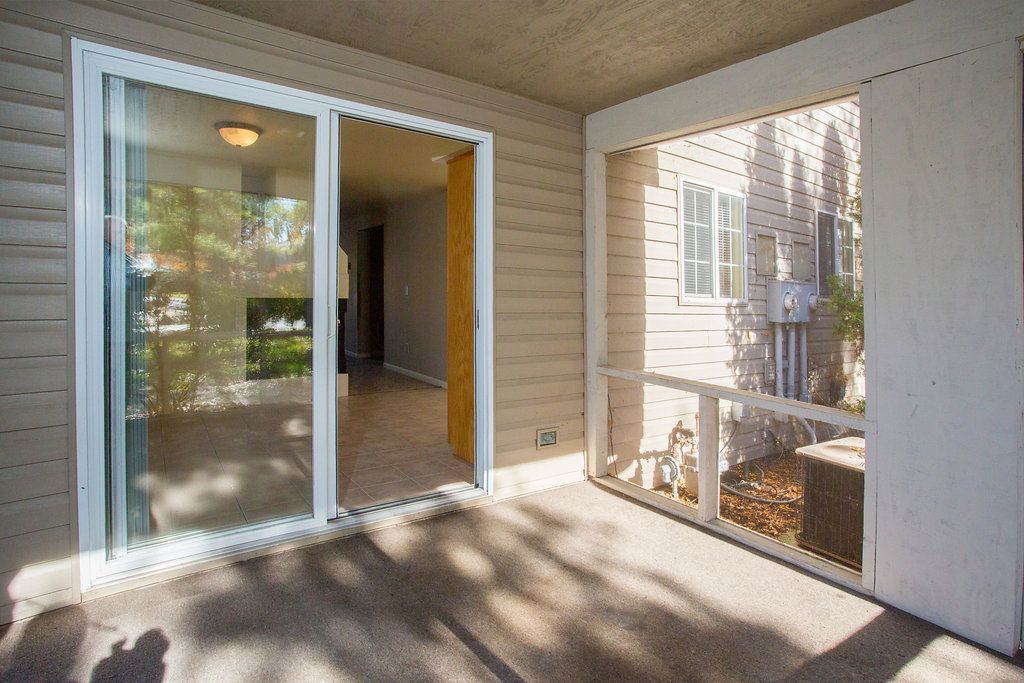 Patio with sliding glass door leading into a room; tan siding and flooring; adjacent screened area.
