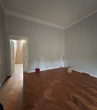 Stanza vuota con pareti grigie, pavimento in legno a spina di pesce e un'apertura che conduce a una scala.
