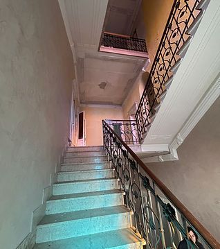 Vano scale interno con ringhiera in metallo e gradini che conducono a un piccolo balcone illuminato dalla luce naturale.