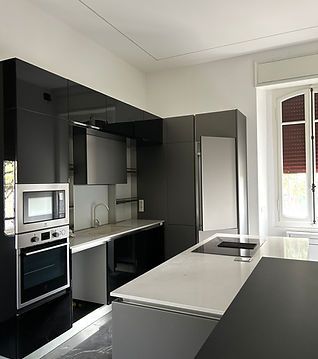 Cucina moderna in bianco e nero con isola, forno a incasso, microonde e frigorifero a colonna vicino a una finestra.