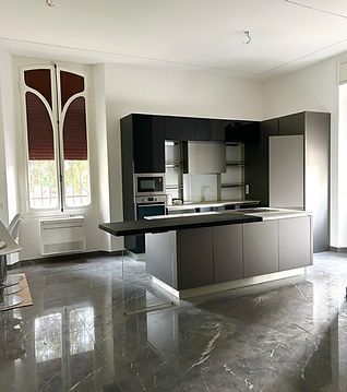 Cucina moderna con mobili scuri, isola centrale, pavimento in marmo grigio lucido e alta finestra ad arco.