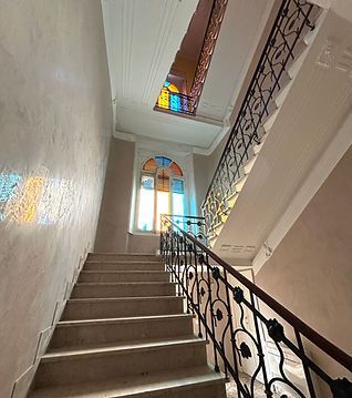 Scala con ringhiera in ferro battuto in un interno luminoso, che conduce a vetrate artistiche.