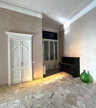 Stanza vuota con pareti beige, porte bianche, pavimento piastrellato e una consolle nera accanto a un vaso verde.