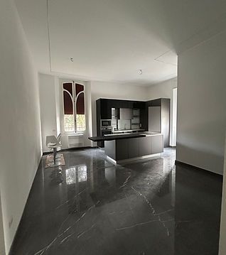 Cucina moderna con isola nera, pavimento scuro lucido, pareti bianche e ampia finestra.
