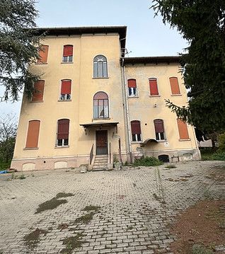 Casa beige a tre piani con persiane rosse e vialetto lastricato, vista dalla facciata principale.