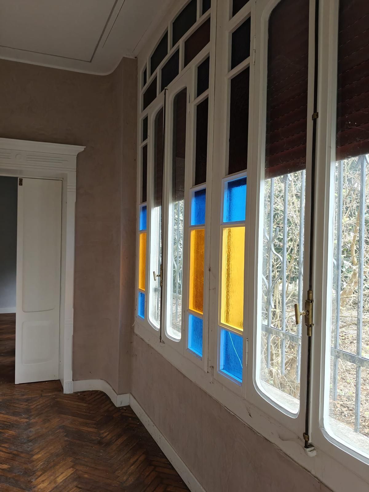 Stanza vuota con alte finestre e decorazioni in vetro colorato blu e giallo lungo la parete.