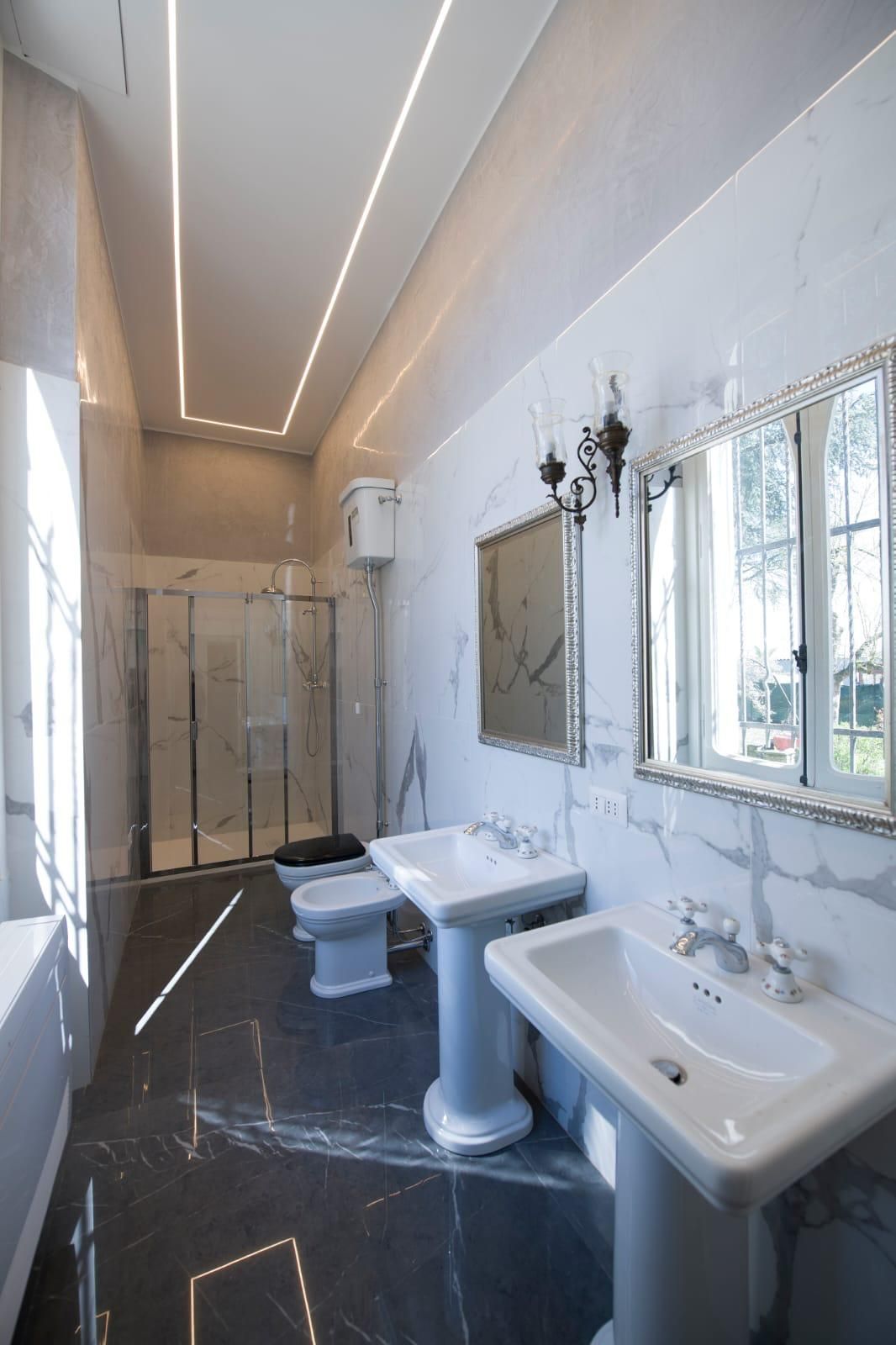Bagno moderno con pavimento in piastrelle nere, sanitari bianchi, specchi e box doccia in vetro.