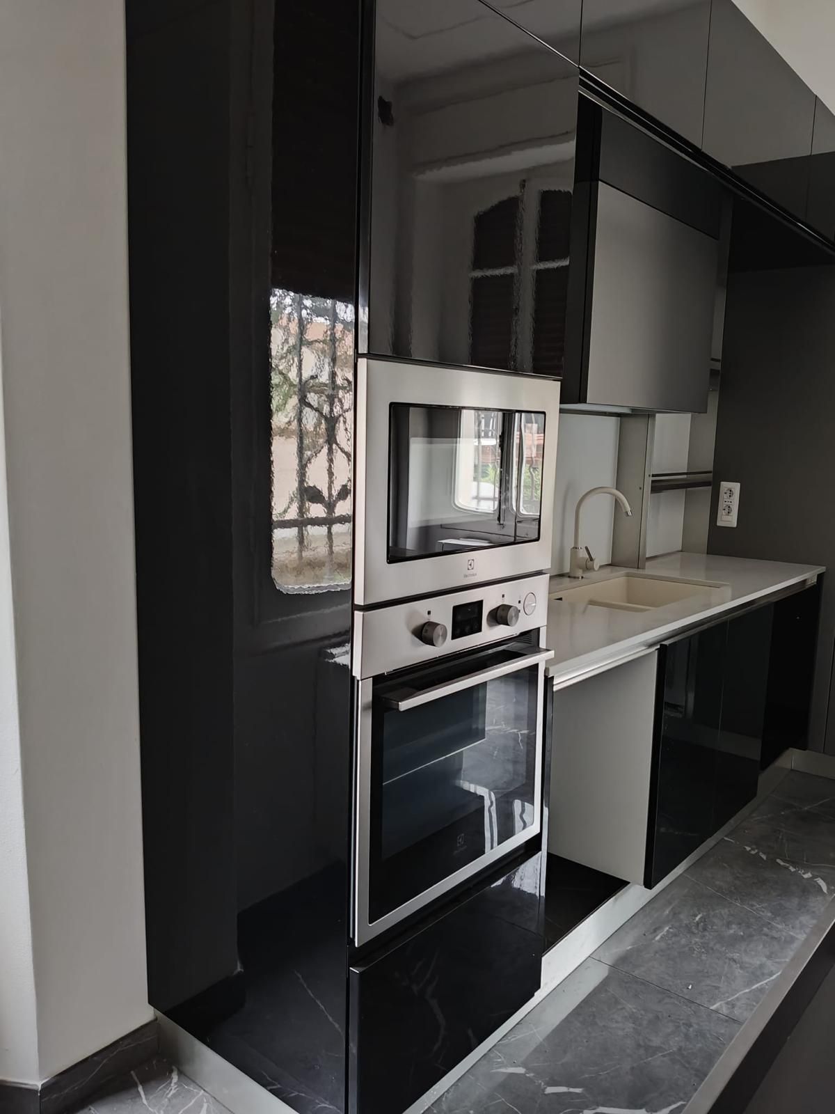 Cucina moderna con mobili neri, ripiani bianchi, forno a incasso, microonde e lavello vicino a una finestra.