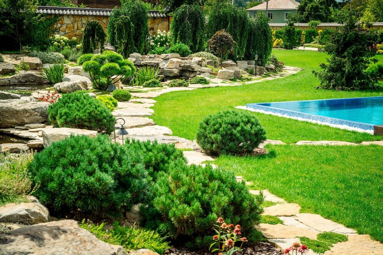 A lush garden with stone pathways, green bushes, and a pool of blue water.