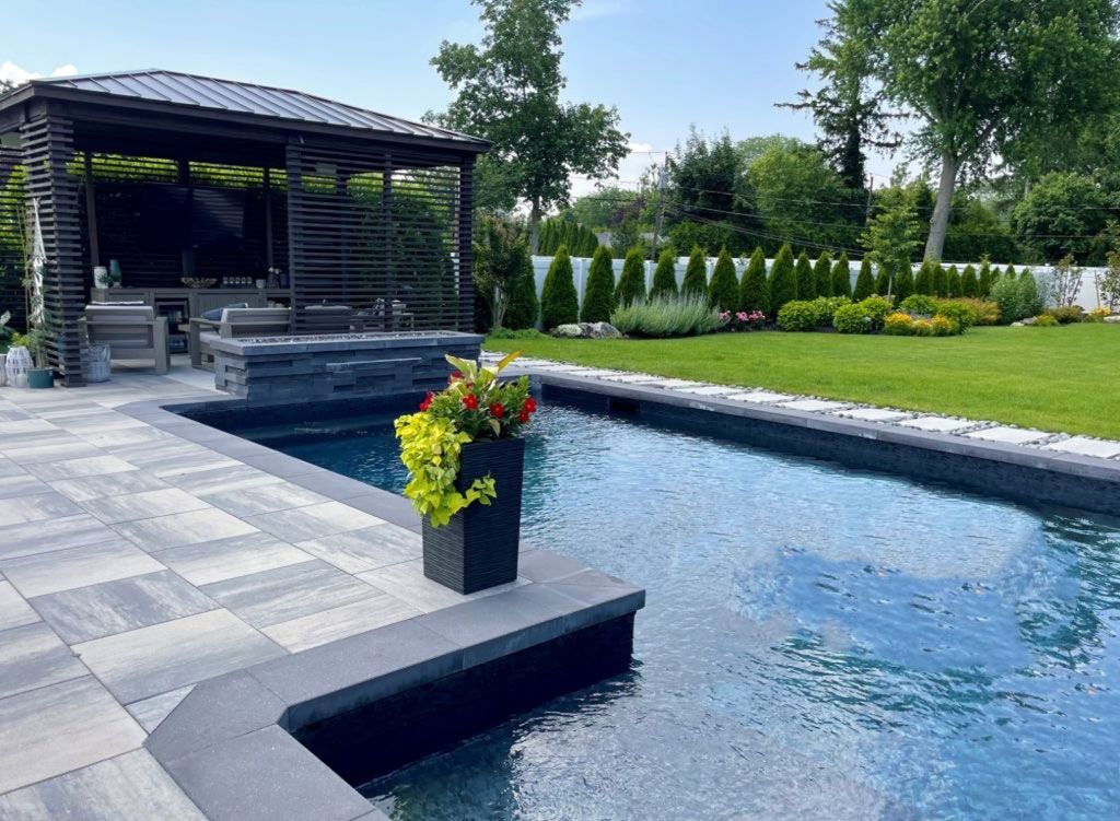 Poolside scene with a gazebo, potted flowers, and lush green lawn.