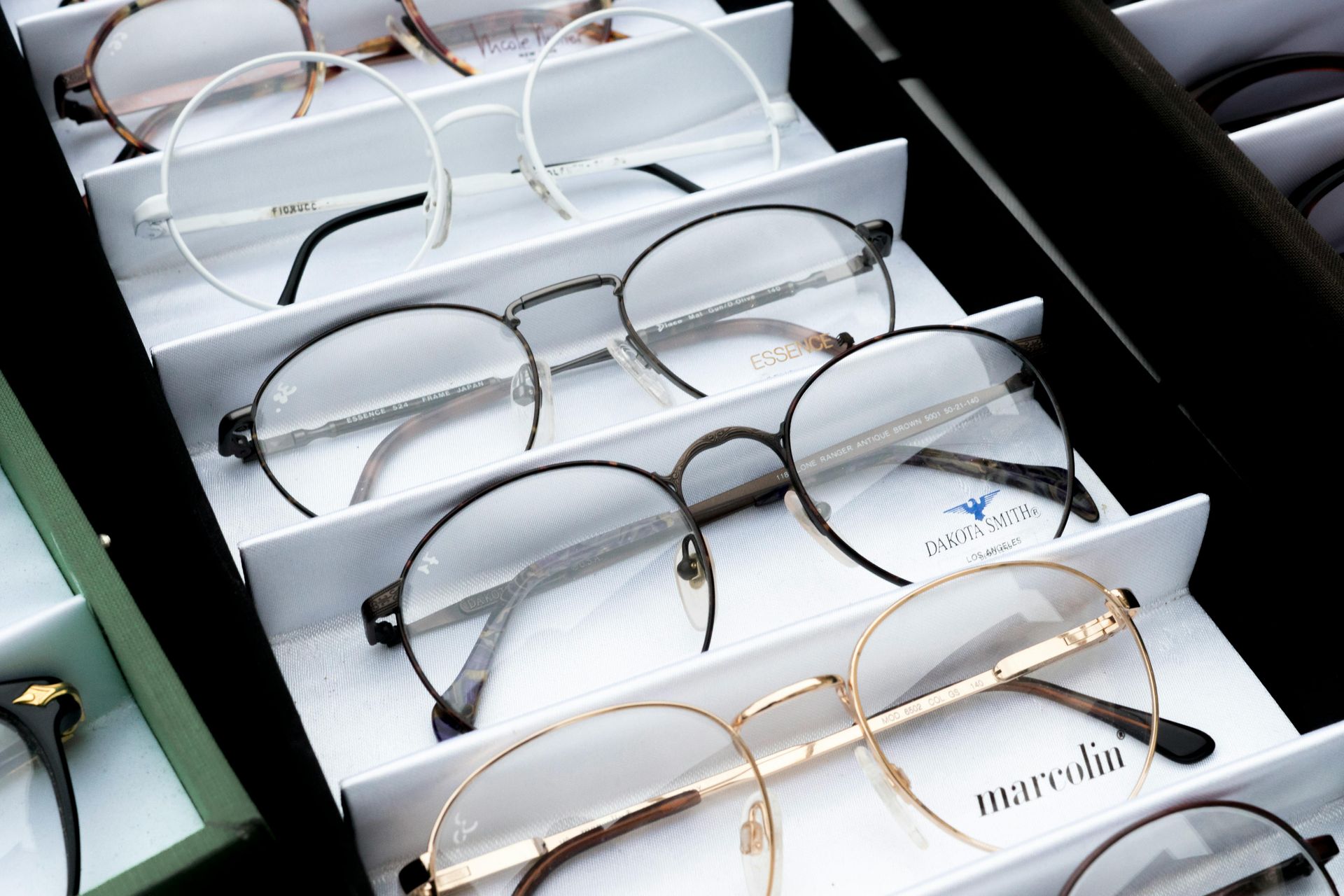Eyeglasses displayed in a white organizer. Various frame styles with black, white, and gold colors.