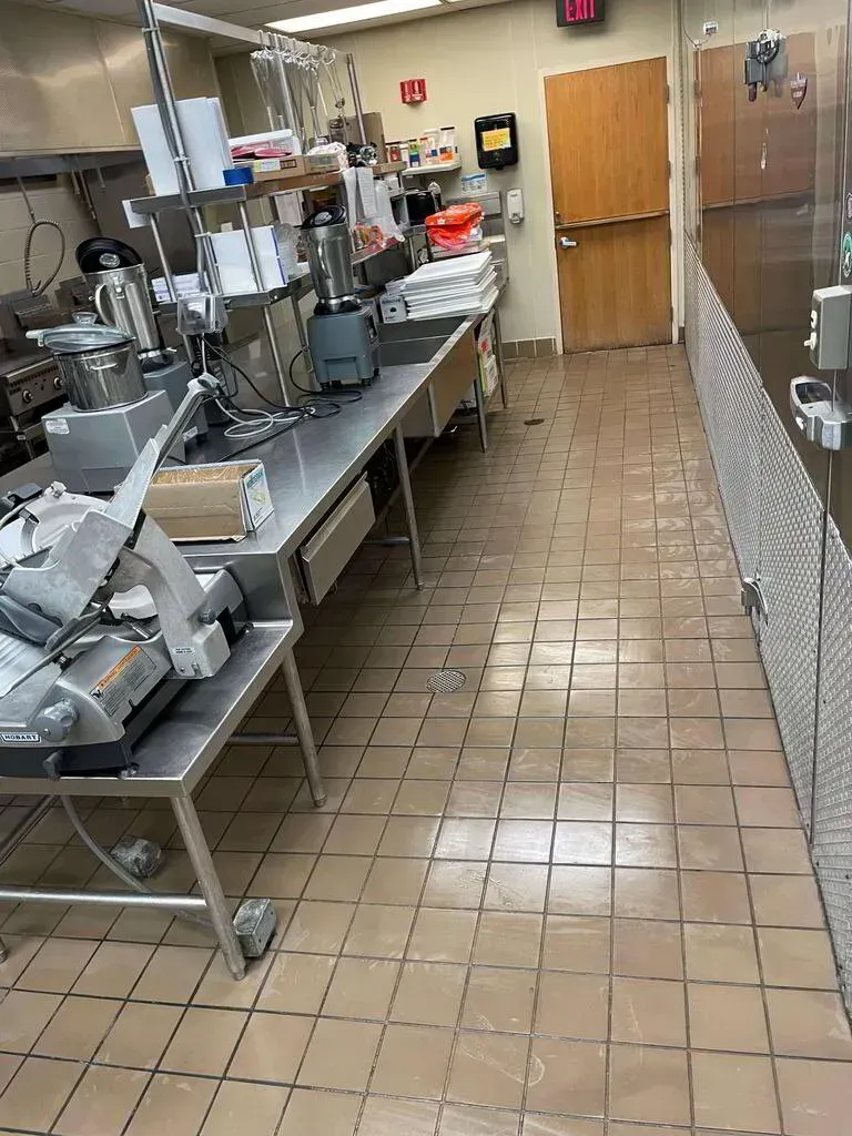Commercial kitchen with stainless steel counters and equipment. Tiled floor, door in the background.