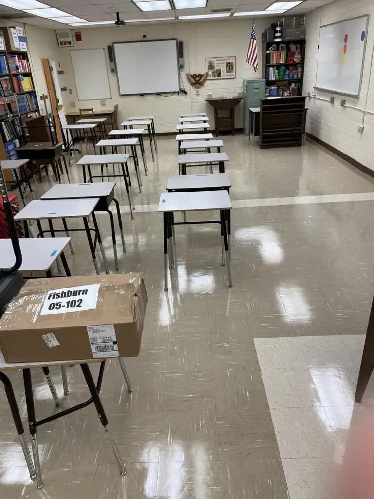 Empty classroom with desks in rows, an American flag, and a box on a desk.