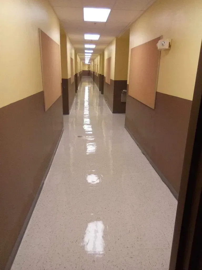 Long, empty hallway with light floor, tan and brown walls, and overhead lights.