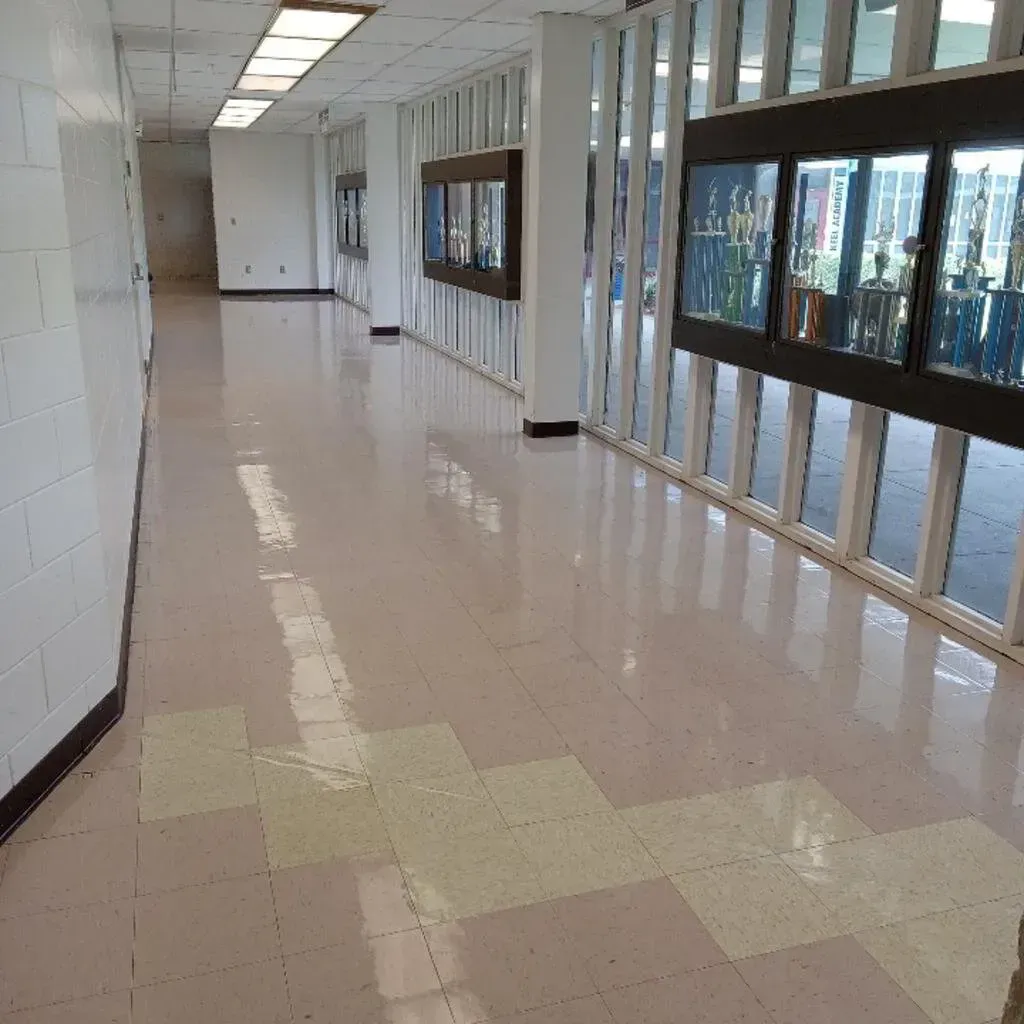 Hallway with glossy pink and cream-colored tiled floor, trophy cases, and white pillars and windows.