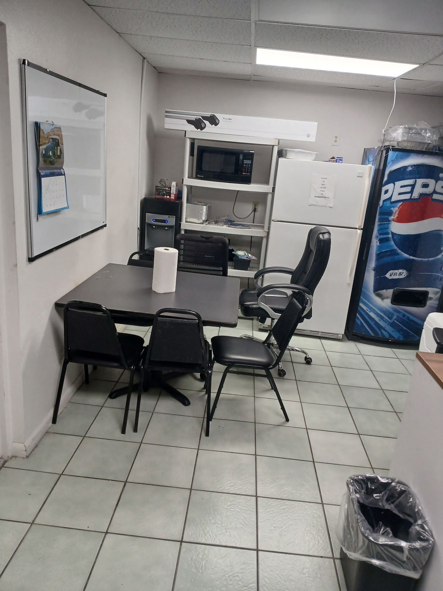 Office space with a table, chairs, a whiteboard, microwave, fridge, and Pepsi machine.
