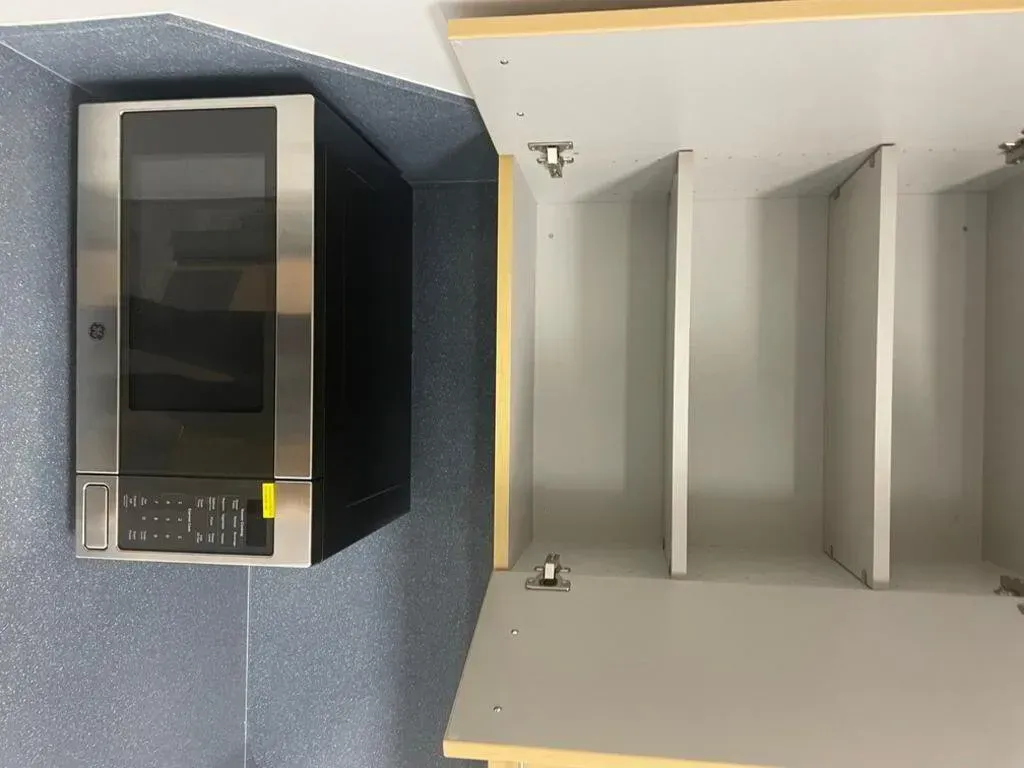 A microwave and an open cabinet with dividers; set in a kitchen with blue speckled walls.