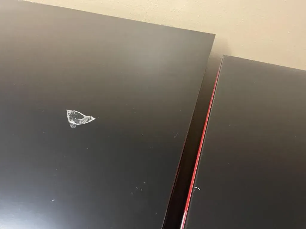 Close-up of two black surfaces with a small white mark, edges separated with a red line, against a beige wall.