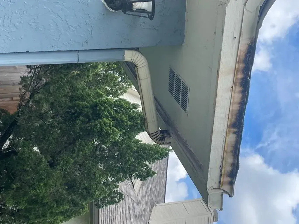 Blue and cream house exterior, gutters, soffit vent, with a tree and partly cloudy sky.