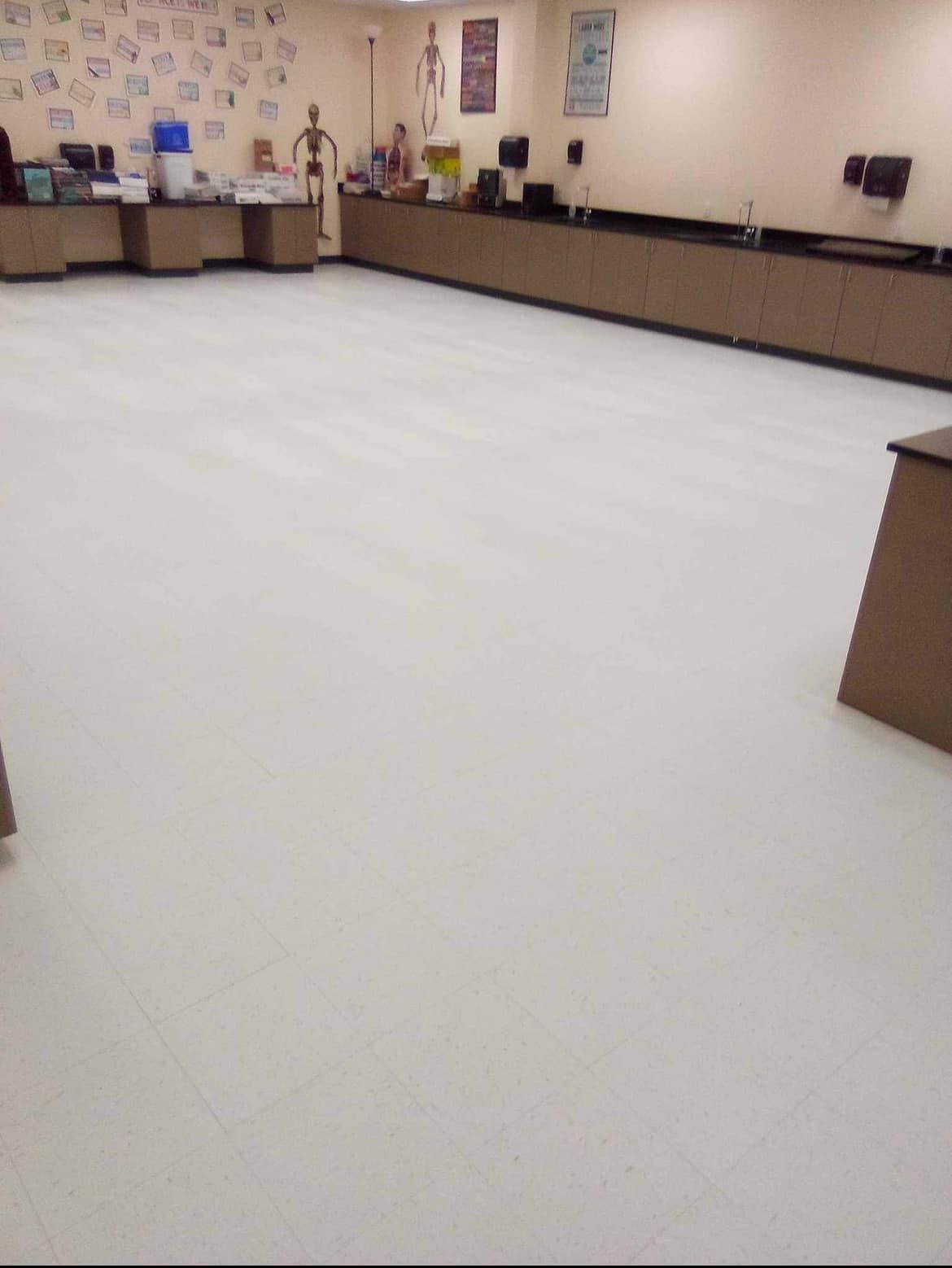 Empty classroom with white tile floor and dark countertops along walls.