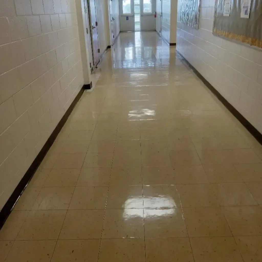 Hallway with beige tiled floor, off-white walls, and doors on the left. Light from the end of the hallway reflects.