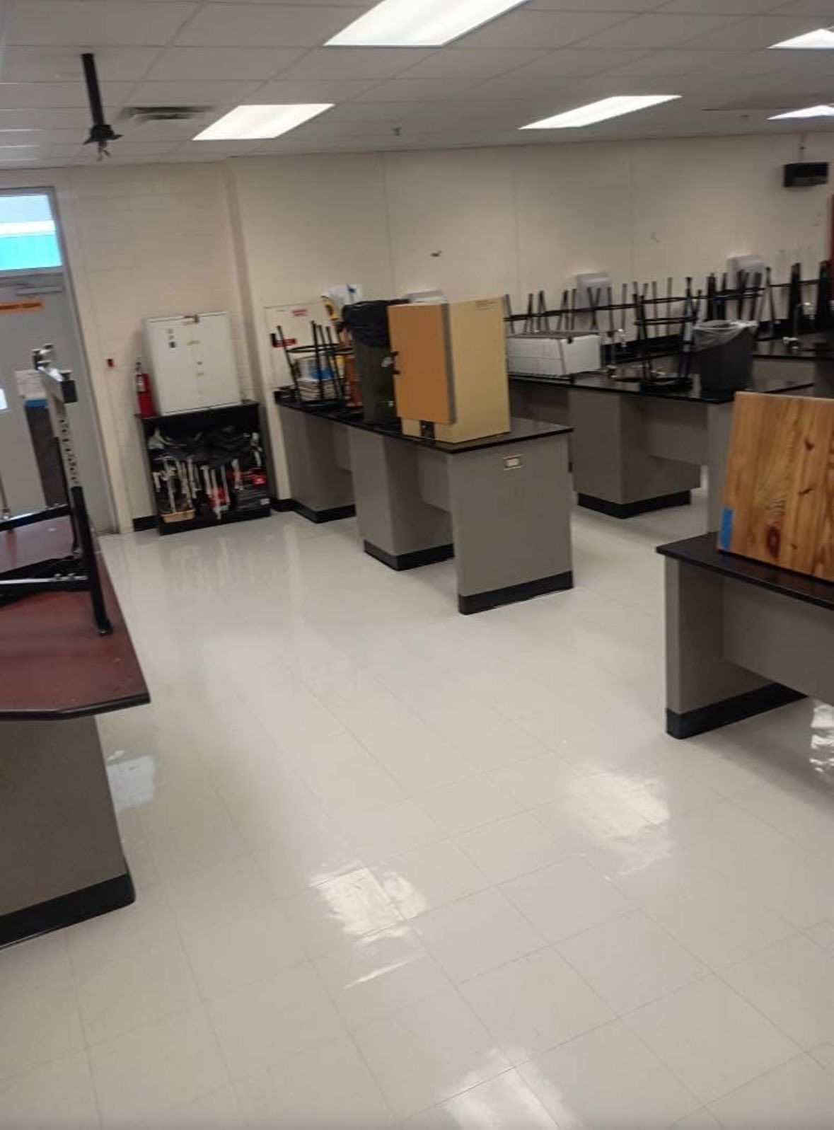 Empty science lab with gray tables, white floor, and tools along the wall.