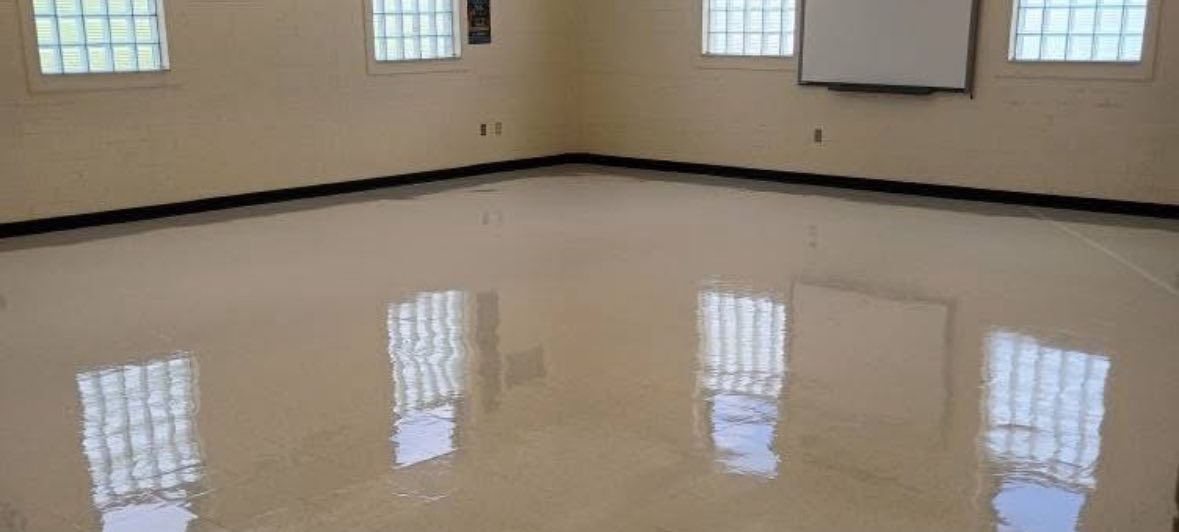 Empty classroom with light-colored floor and dark brown counters. A skeleton model is visible in the background.
