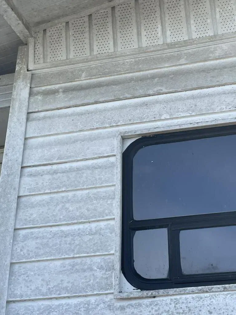 Gray siding of a building with a window and a roof edge with small holes.