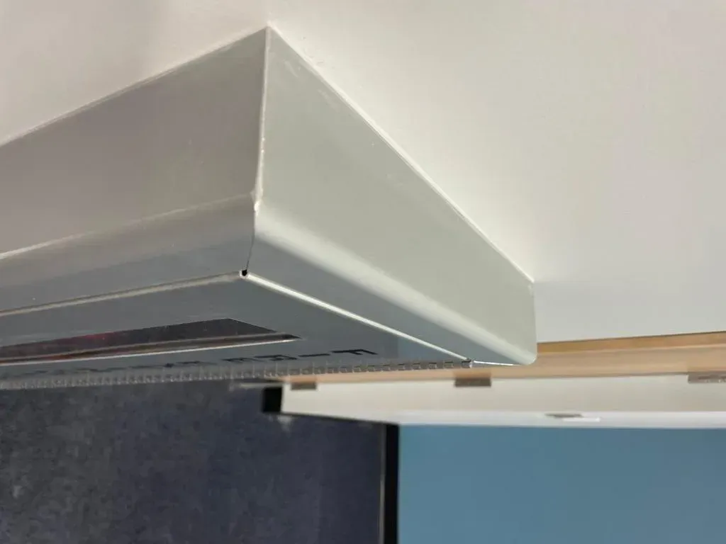 Silver range hood mounted above a black appliance. White walls and wooden trim are visible.