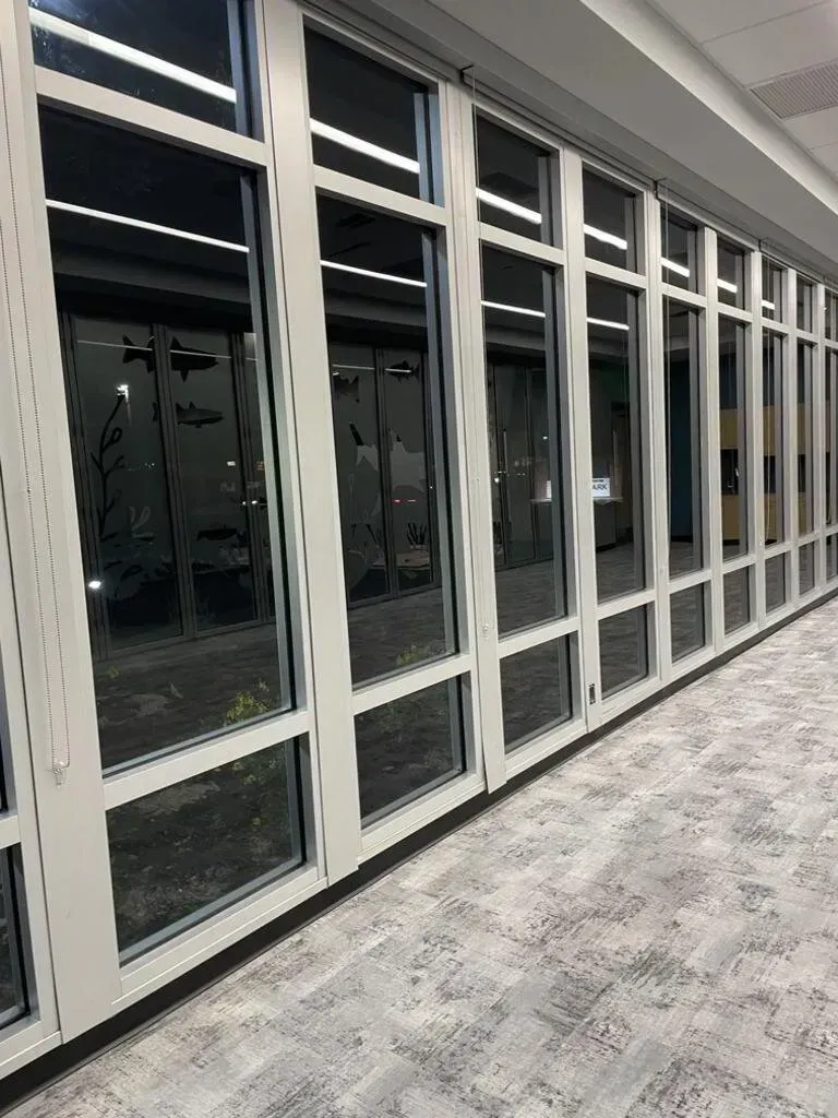 A row of large, white-framed glass windows along a hallway with gray carpeting; interior view.