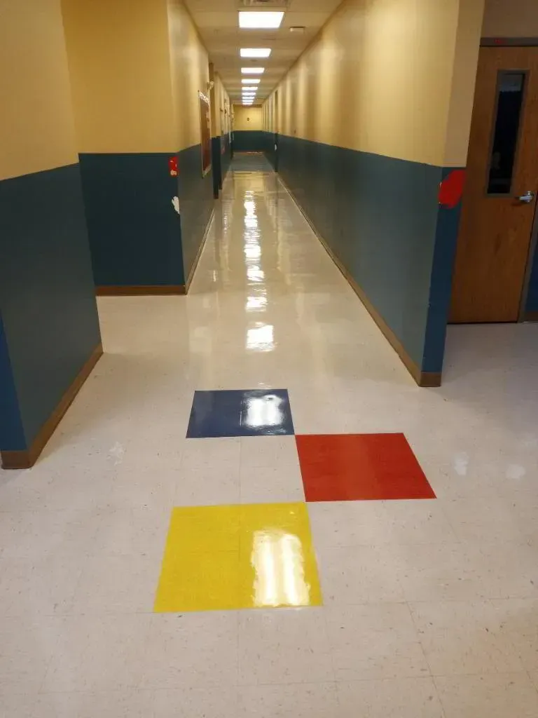 Hallway with blue, yellow, and red squares on the floor, blue and cream walls, and a long, straight perspective.