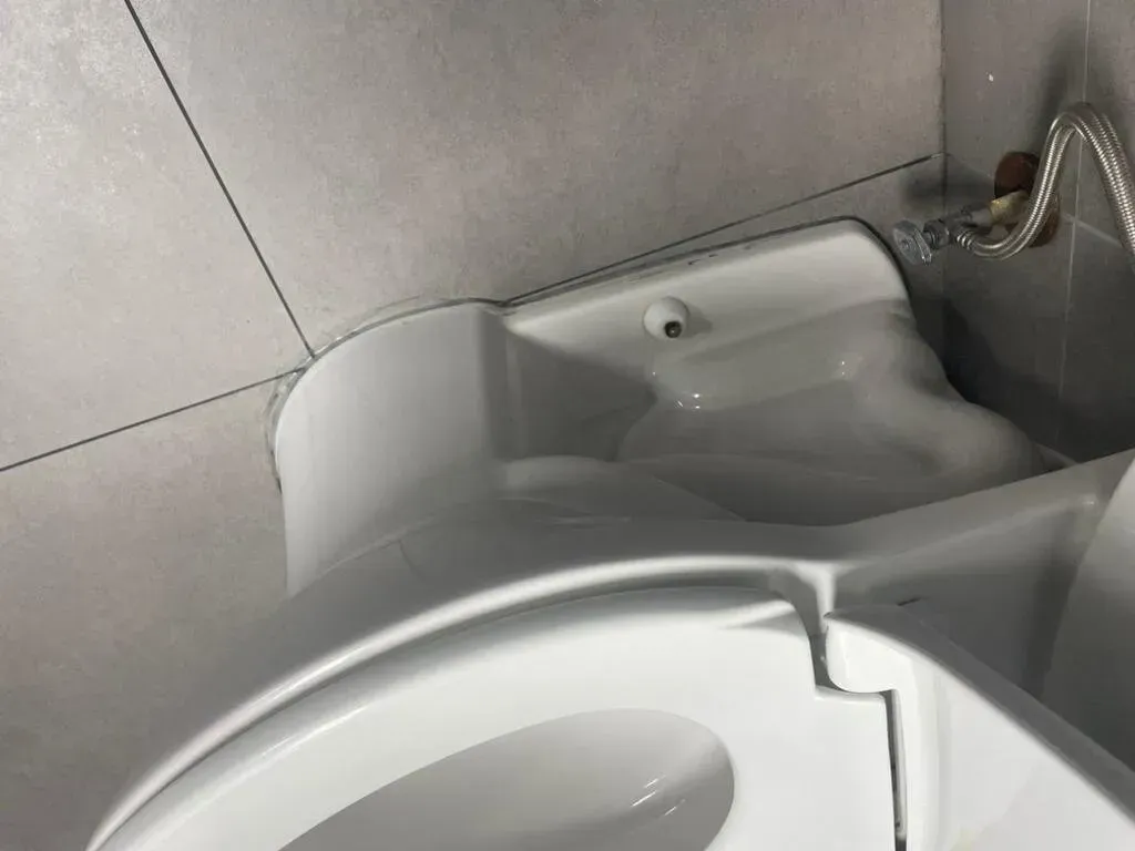 White toilet against gray tiled wall, with water supply pipe visible.