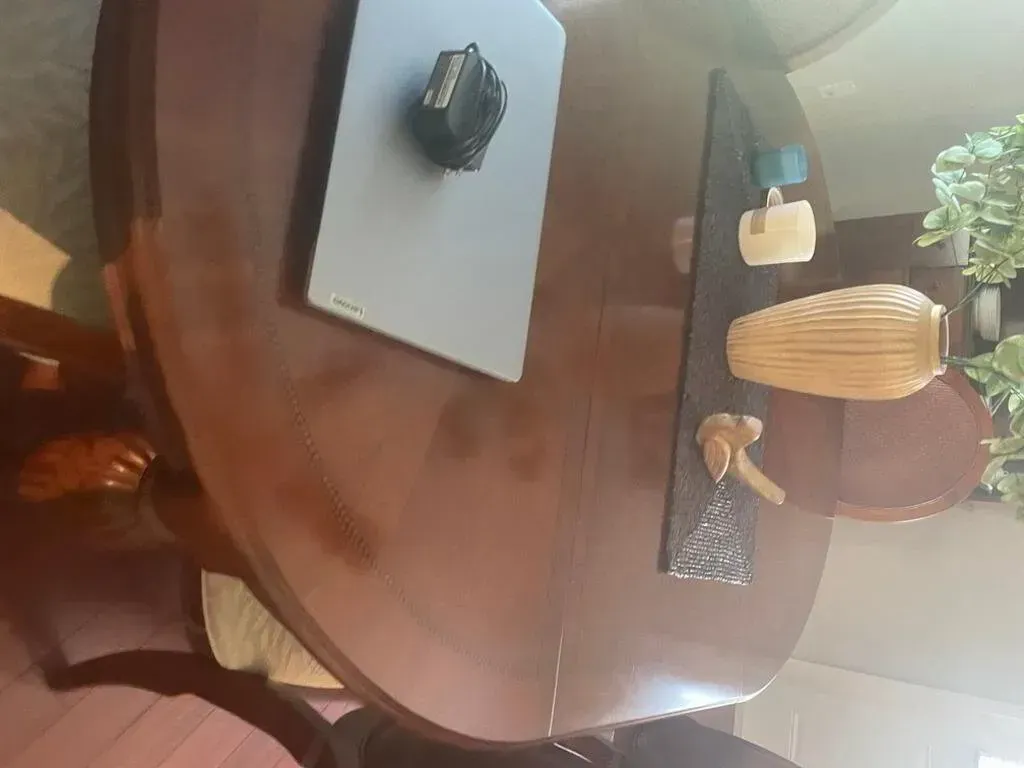 Round wooden dining table with decorations, including a vase and a black object on a blue mat.