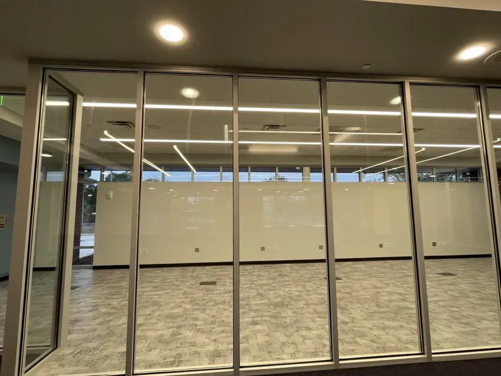 Glass-walled room with neutral carpet and white walls. Silver frames divide the glass panels; lights shine from the ceiling.
