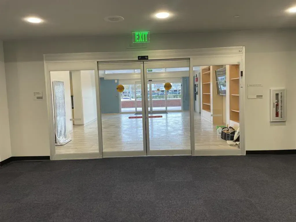 Automatic sliding glass doors, leading to a brightly lit room. 