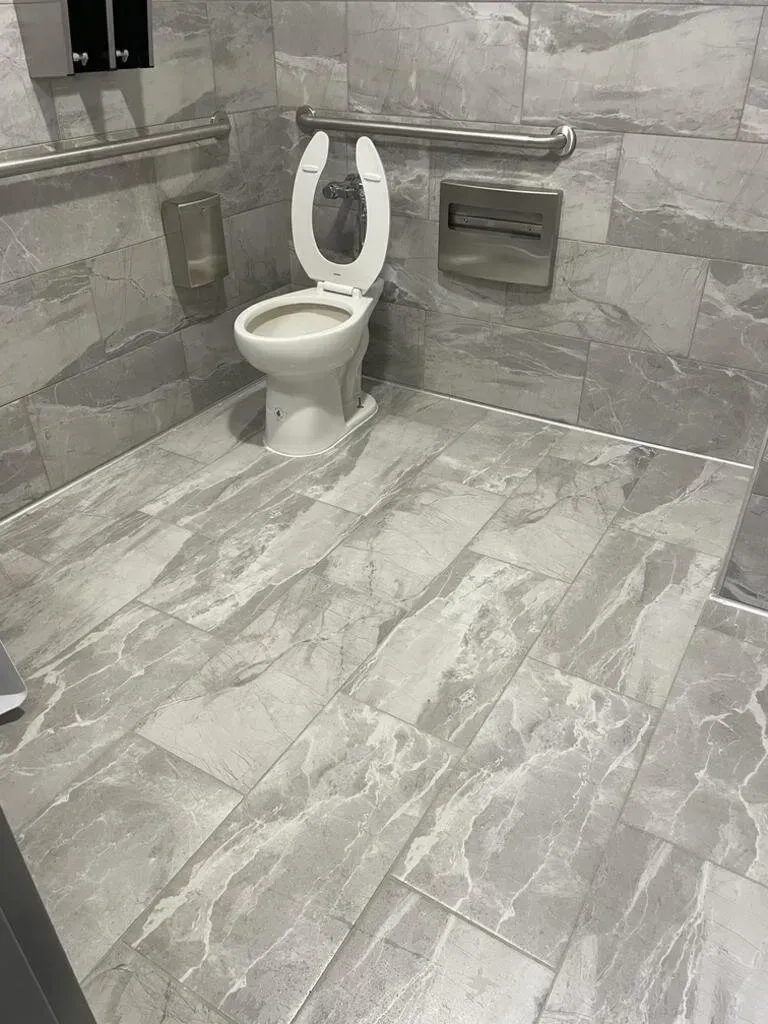 ADA accessible restroom with a toilet, grab bars, and neutral gray tile.