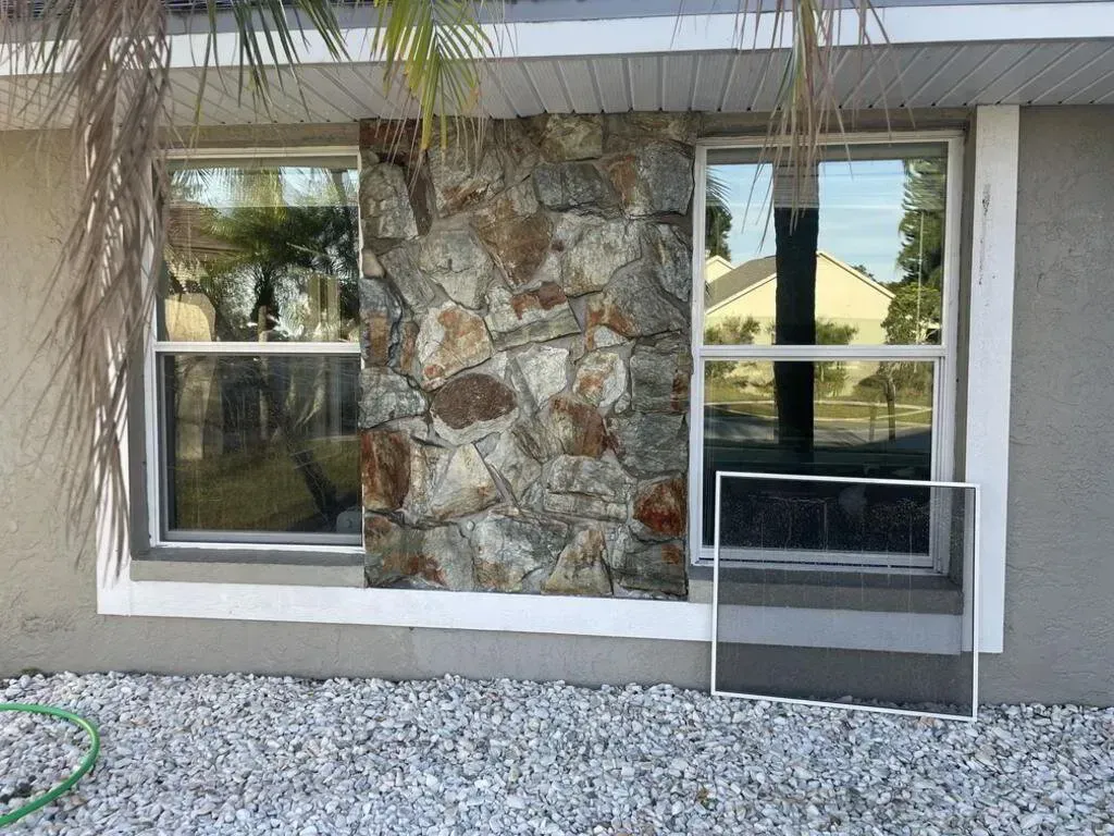 Exterior of a house with two windows flanking a stone accent wall. A detached screen sits in front.