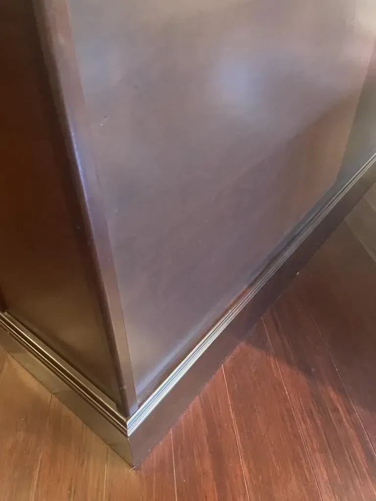 Dark brown corner cabinet, with a shiny, reflective surface, on a dark wooden floor.