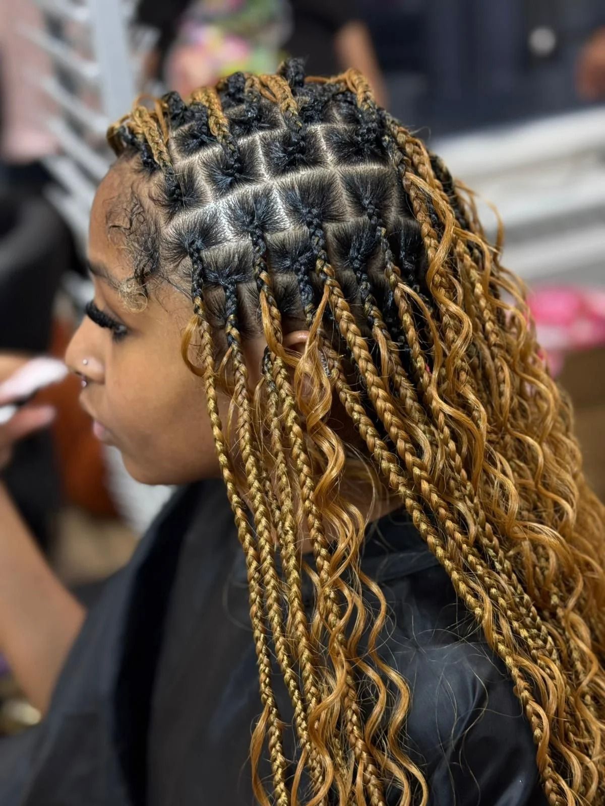 Side-profile close-up of a braided hairstyle with black roots and blonde twists in a salon chair