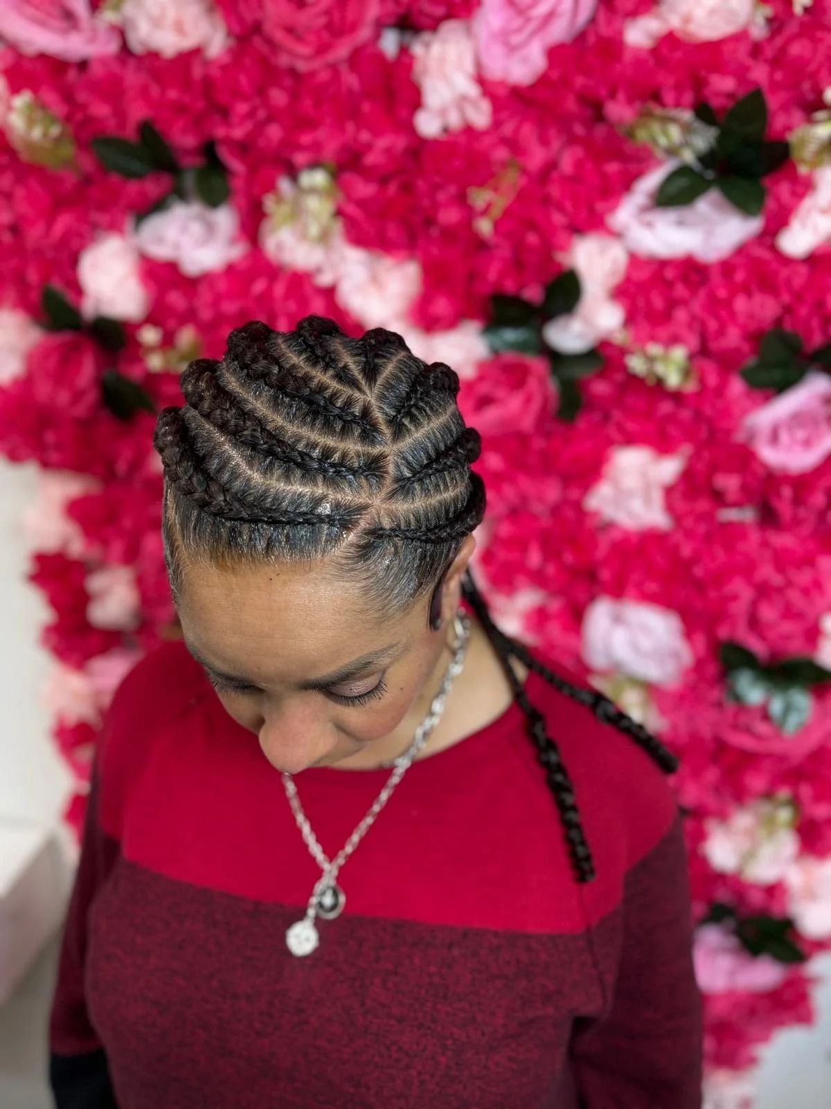Woman with braided hair in a burgundy top, looking down against a bright pink floral backdrop