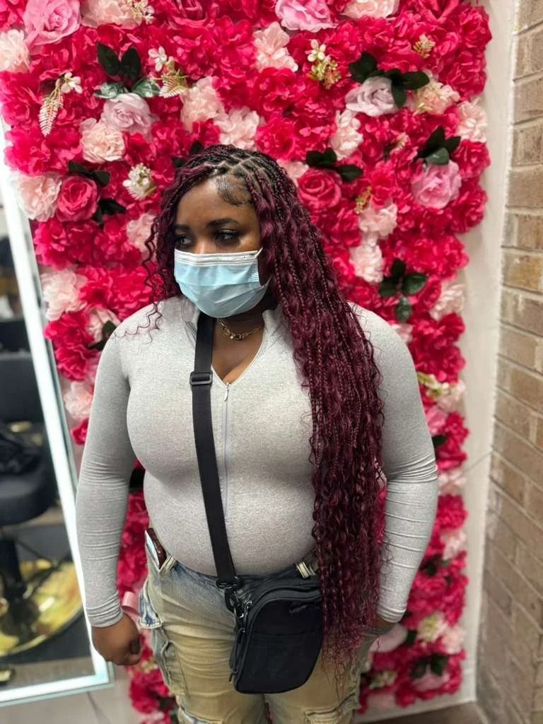 Woman wearing a face mask and gray top, standing in front of a pink floral wall.