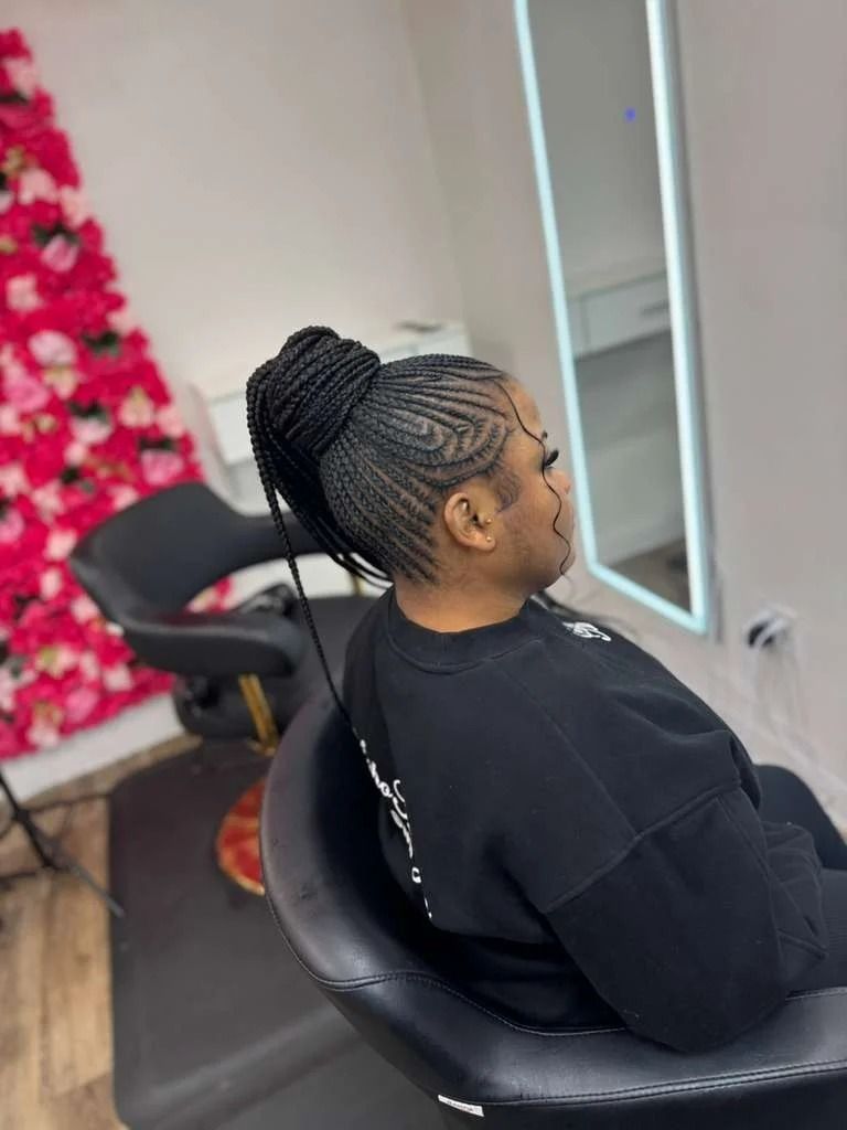 Person with braided updo sitting in a salon chair near a mirror and pink floral decor