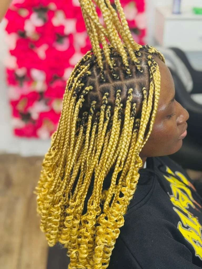 Close-up of braided hair with yellow ombré twists over a black shirt against a pink floral background