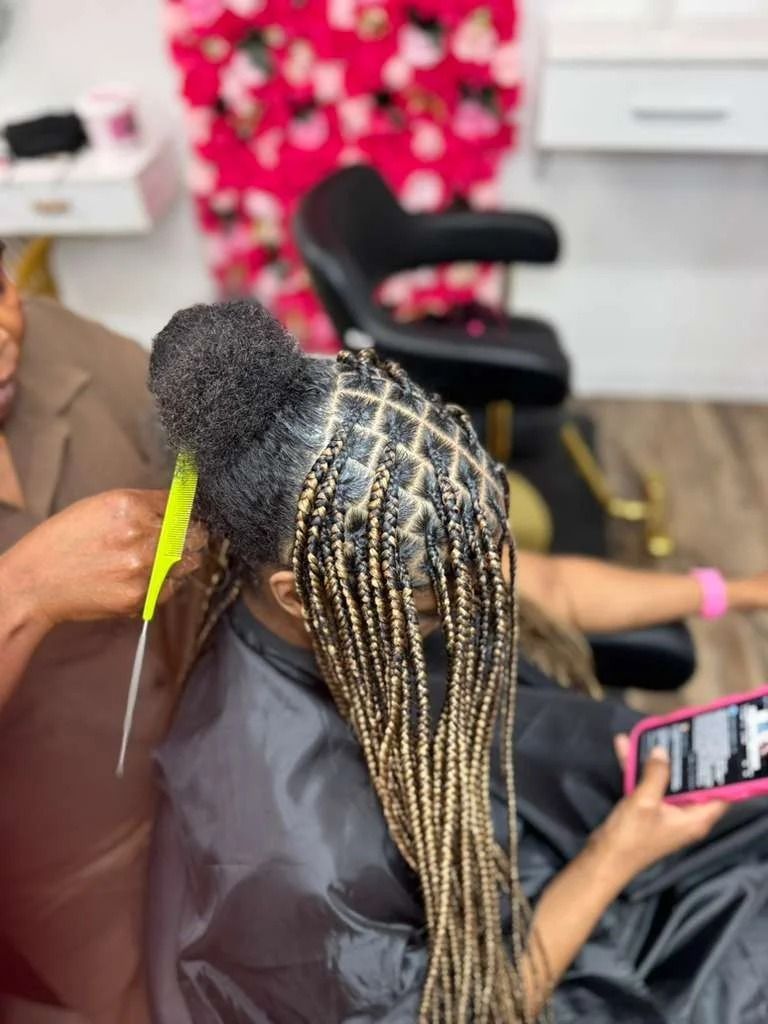 Braided hairstylist at work, showing long blonde and black box braids in a salon chair