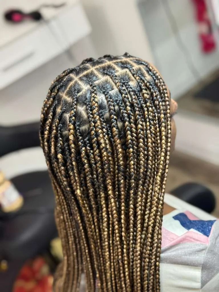 Close-up of long black and blonde braided hair styled in neat rows at a salon chair