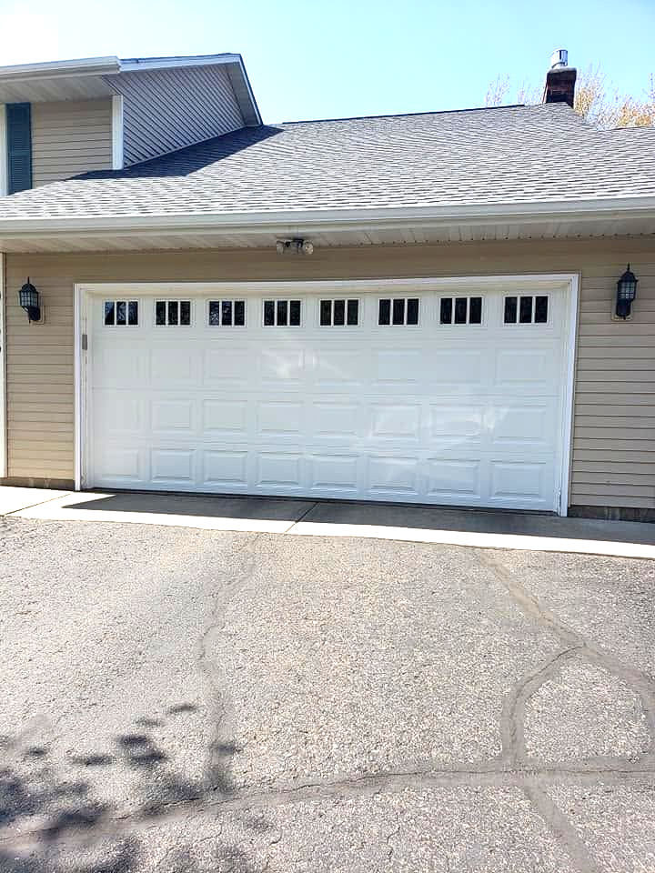 Suburban house with a white garage door and gray shingle roof under a clear blue sky